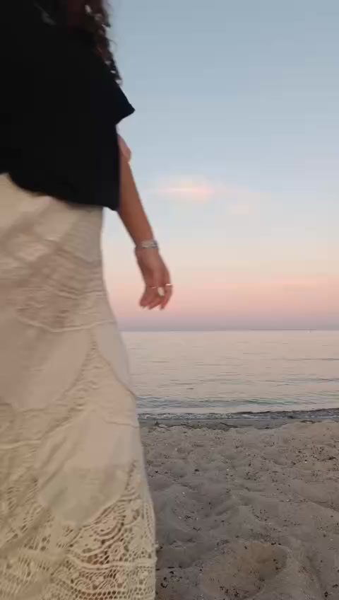 En kvinde på stranden ved solnedgang i en sort Nevani t-shirt.