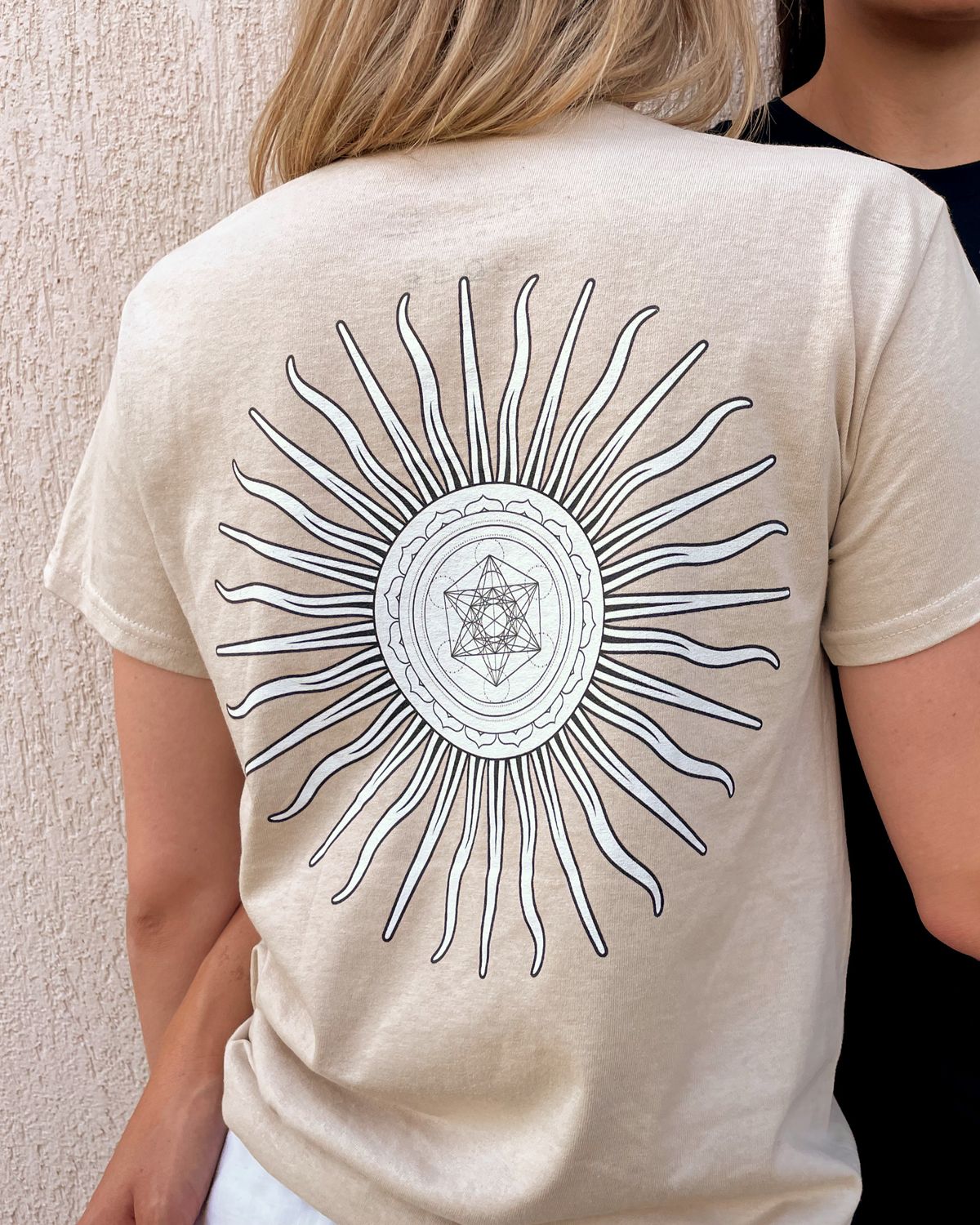 En person set bagfra i en sandfarvet t-shirt med Metatrons terning sol.
